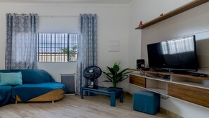 A modern living room with a teal sofa, a flat-screen TV, and a small side table. - Casa em Peruíbe a 250m da Praia com Piscina (Peruíbe)