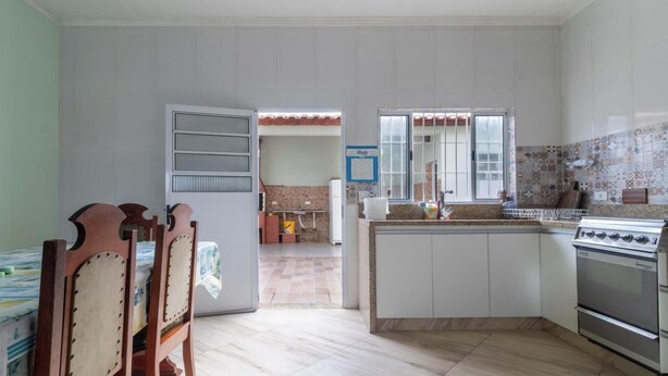A compact kitchen with a dining area, a refrigerator, a stove, and a tiled backsplash. - Casa em Peruíbe a 250m da Praia com Piscina (Peruíbe)