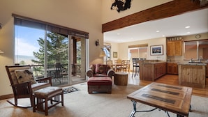 A spacious living area with a large sliding glass door leading to a balcony, a wooden dining table, and a kitchen with wooden cabinets and a stone island. - Midway 4 Bedroom Golf Course Luxury Turnberry 23 Home (Midway)