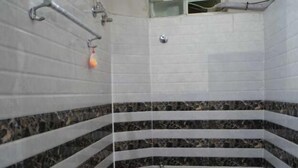 Un baño pequeño con paredes de azulejos blancos, suelo de mármol, inodoro blanco y zona de ducha con puerta de cristal.