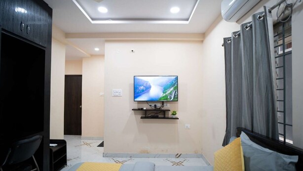 Un dormitorio moderno con televisión montada en la pared, cama con colcha amarilla y azul, y un armario de color oscuro.