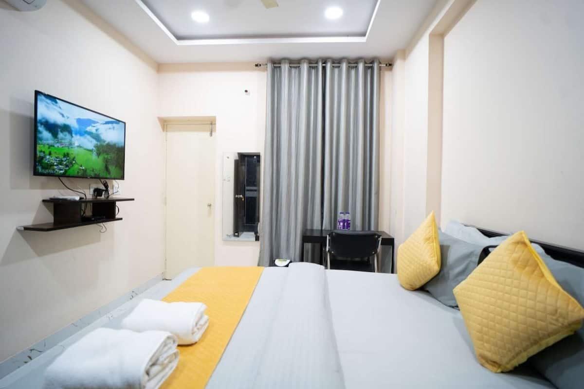 Une chambre d’hôtel avec un lit, un téléviseur fixé au mur, une petite table avec une chaise et une fenêtre avec des rideaux.