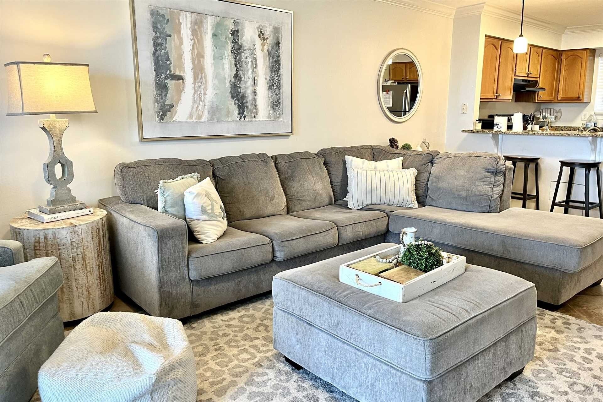 A living room with a grey sectional sofa, a matching ottoman, a coffee table, a lamp, and a painting on the wall.