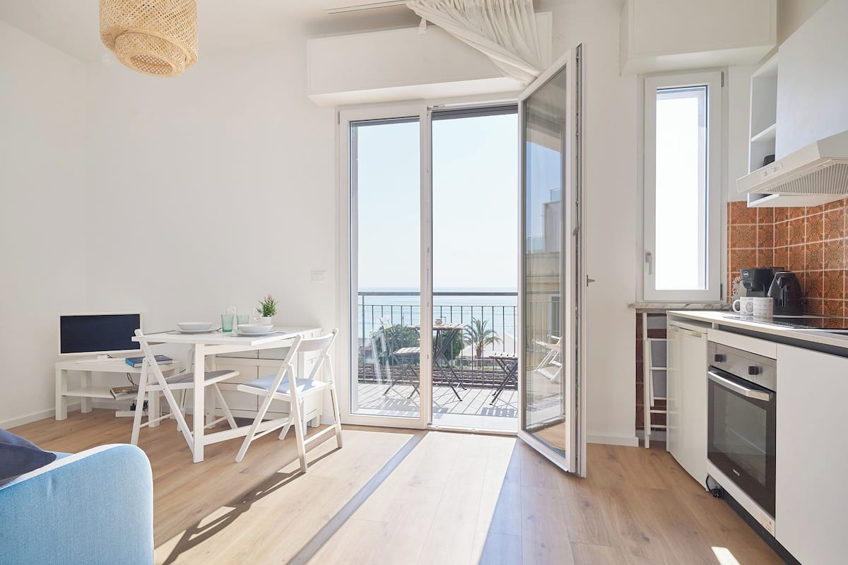 Une cuisine moderne dotée d’une grande fenêtre, un coin repas avec une table et des chaises, et une vue sur la mer.