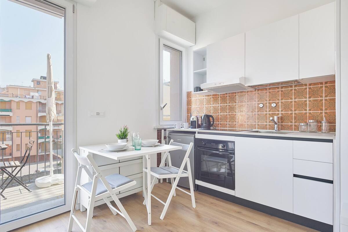 Une cuisine moderne avec des meubles blancs, un four noir et un pare-feu en carreaux.