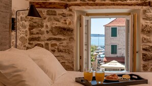 A bed with pillows, a tray with croissants, juice, and a glass of orange juice, and a view of a building with a red roof through a window. - Suite in the heart of the city, just a few meters from the sea (Kaštel Stari)