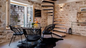 A dining area with a stone wall, a spiral staircase, and a glass table with chairs. - Suite in the heart of the city, just a few meters from the sea (Kaštel Stari)