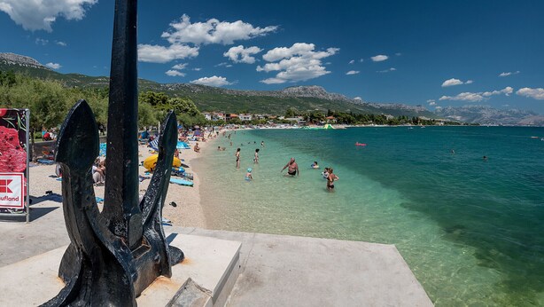 A beach with clear water, people swimming, and a large black sculpture in the foreground. - Suite in the heart of the city, just a few meters from the sea (Kaštel Stari)