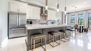 Una cocina moderna con un refrigerador de acero inoxidable, gabinetes blancos, una encimera de mármol y taburetes de bar.