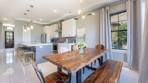 Una cocina moderna con armarios blancos, una mesa de comedor de madera y luces colgantes.
