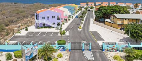 A coastal road with colorful buildings, a gated entrance, and a view of the ocean.