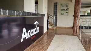 Un espace d’accueil d’hôtel avec une enseigne indiquant « Hôtel Acacia » et des panneaux de signalisation indiquant « Ekoomi Club », « Salle de conférence Ishaazi » et « Salle de sport ».