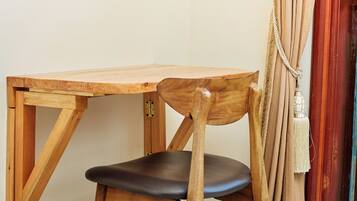 A wooden table and chair with a simple design, positioned against a plain wall with a curtain partially visible.