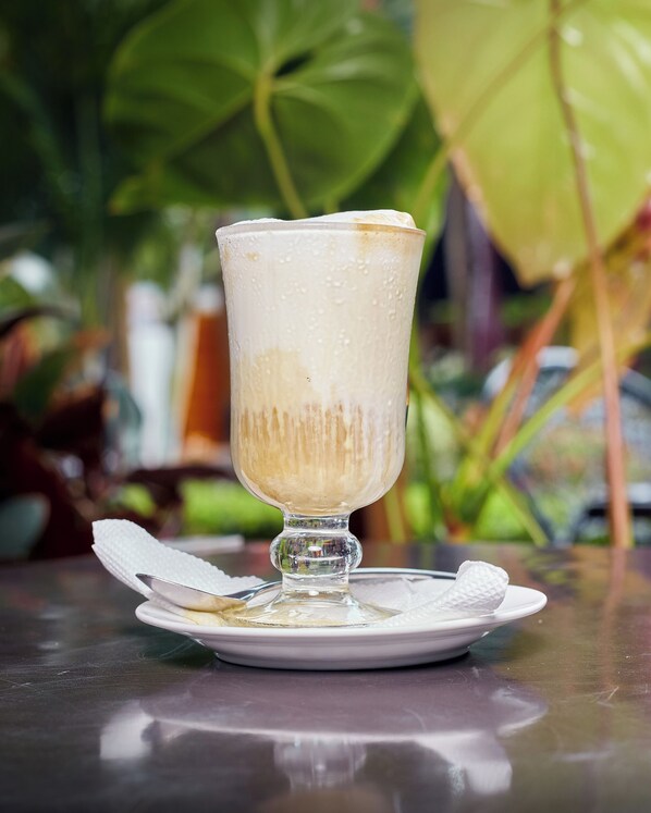 Un vaso de café helado sobre un plato blanco con una servilleta, sobre una superficie reflectante.