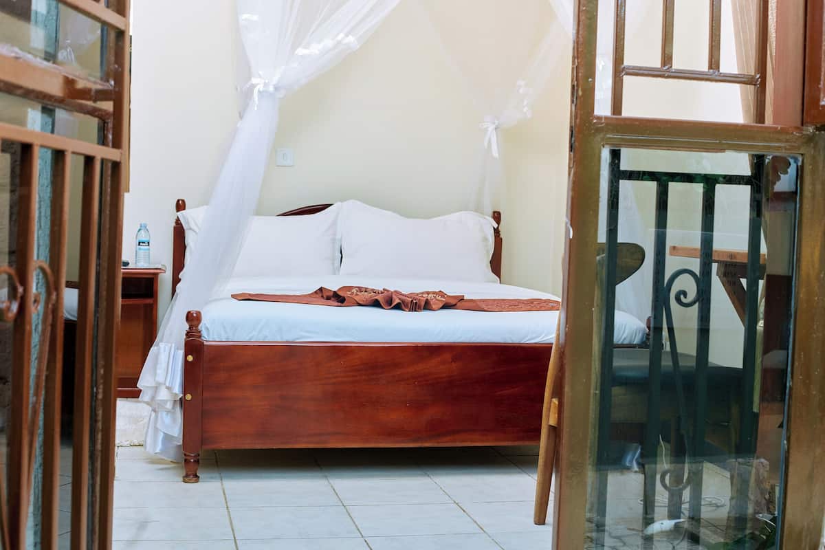 A wooden bed with white linens, a bedside table with a water bottle, and a glass door leading to another room.