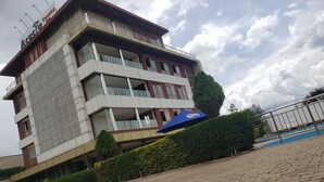 Un hôtel à plusieurs étages, doté de balcons, d’un parasol bleu et d’une zone pavée devant l’entrée.