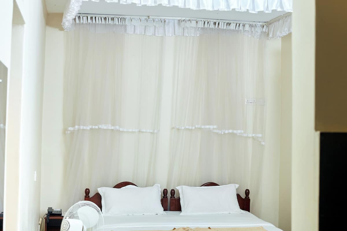 A bed with a canopy, a bedside fan, and a telephone on a nightstand.