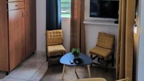 Une pièce comprenant une armoire en bois, deux fauteuils, une petite table ronde et un téléviseur fixé au mur.