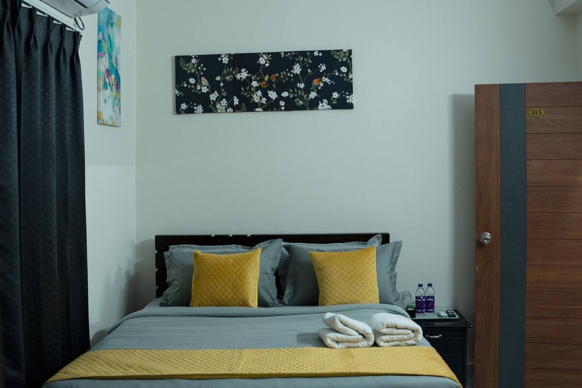 A neatly arranged bedroom with a bed, a ceiling fan, a wall-mounted air conditioner, and a door with a number.