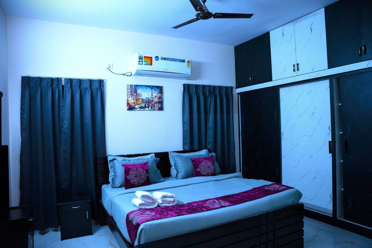 A bedroom with a bed, air conditioning unit, curtains, a ceiling fan, and a wardrobe.