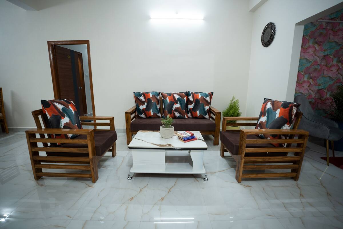 A living room with a sofa, two wooden chairs, a coffee table, and a door.