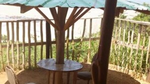 A covered outdoor seating area with a table and chairs, surrounded by a wooden fence and a view of greenery.