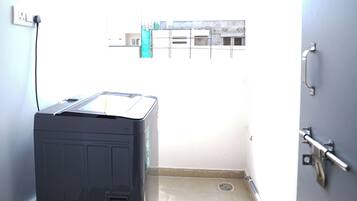 A laundry room with a large industrial washer and dryer, a window with a view of buildings, and a door with a handle.