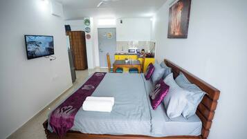 Een slaapkamer met een bed, een televisie en een kitchenette op de achtergrond.