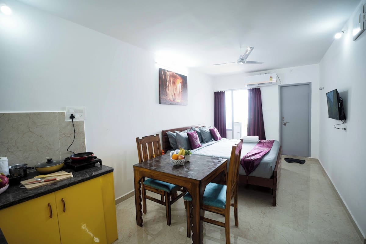 Una habitación pequeña con cama, mesa de comedor y kitchenette.