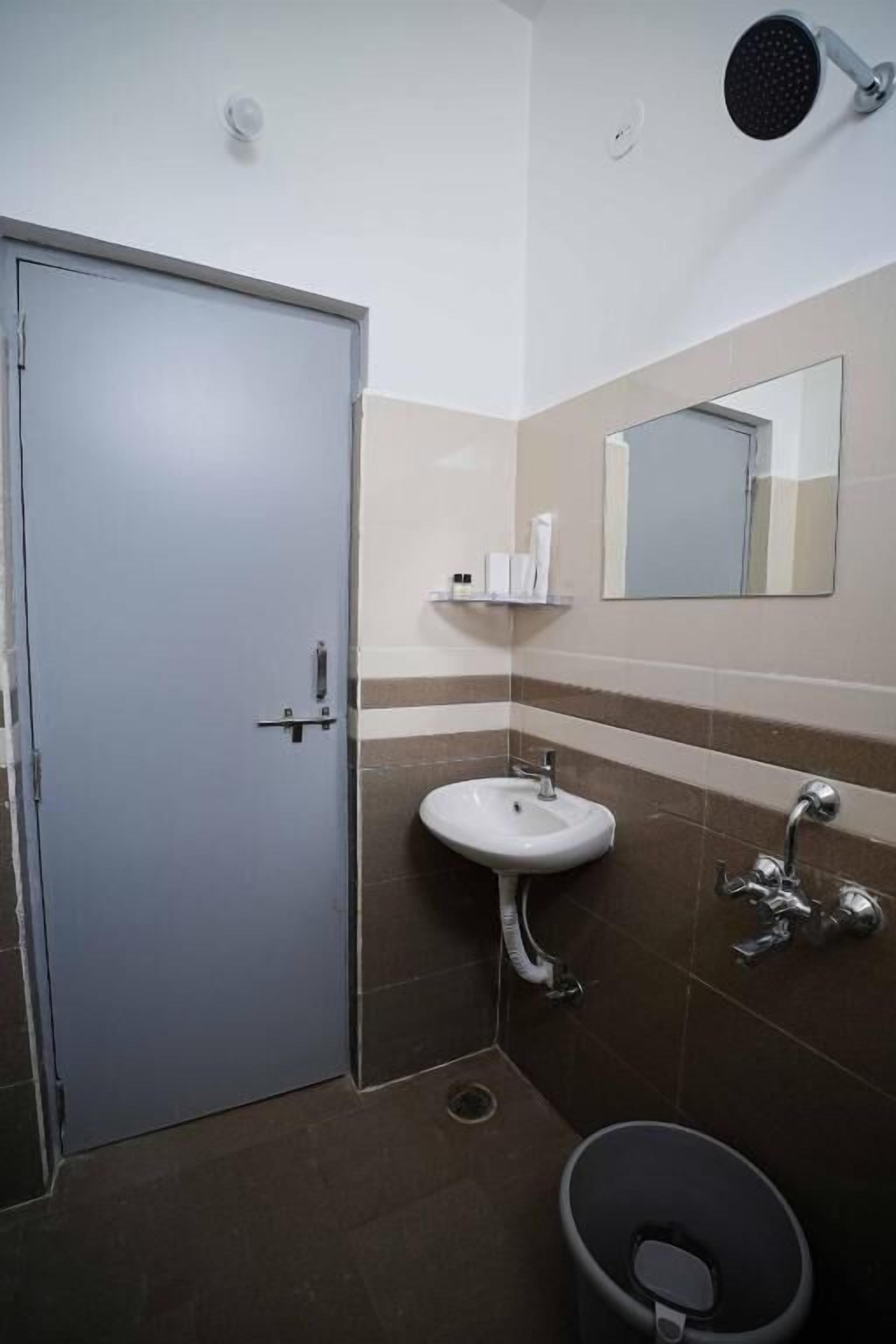 Un baño con lavamanos blanco, un espejo, un cabezal de ducha y un inodoro.