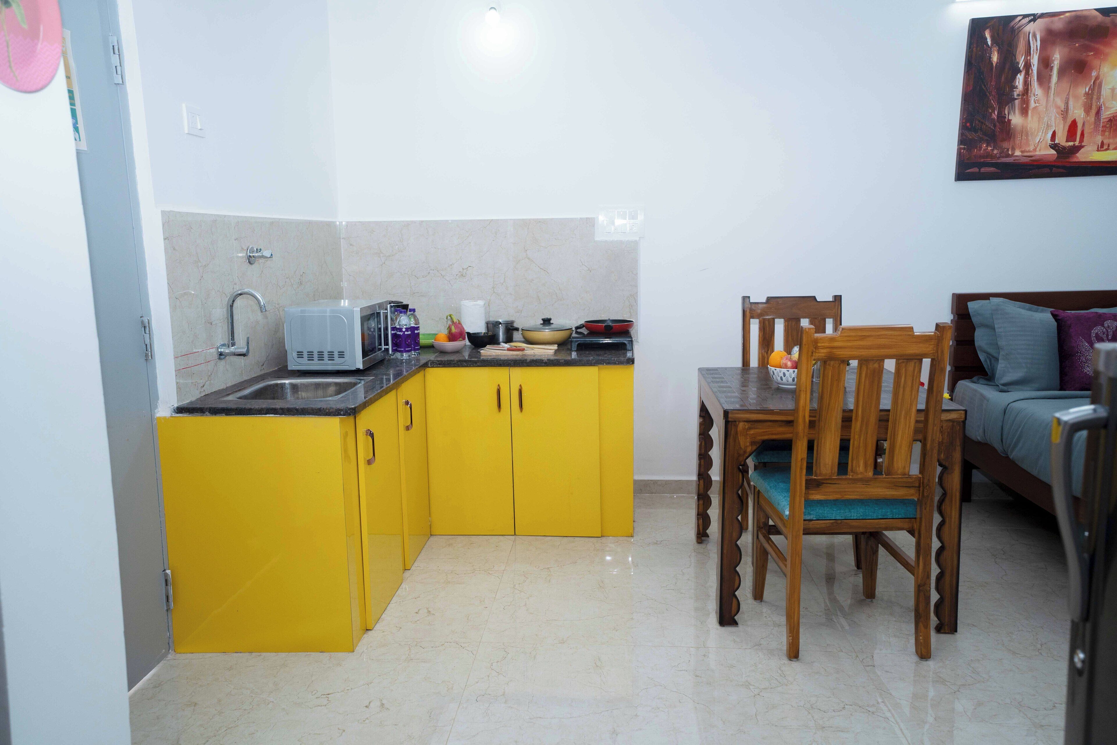 A compact kitchen with yellow cabinets, a microwave, and a sink. There is a dining table with chairs and a sofa in the adjacent living area.