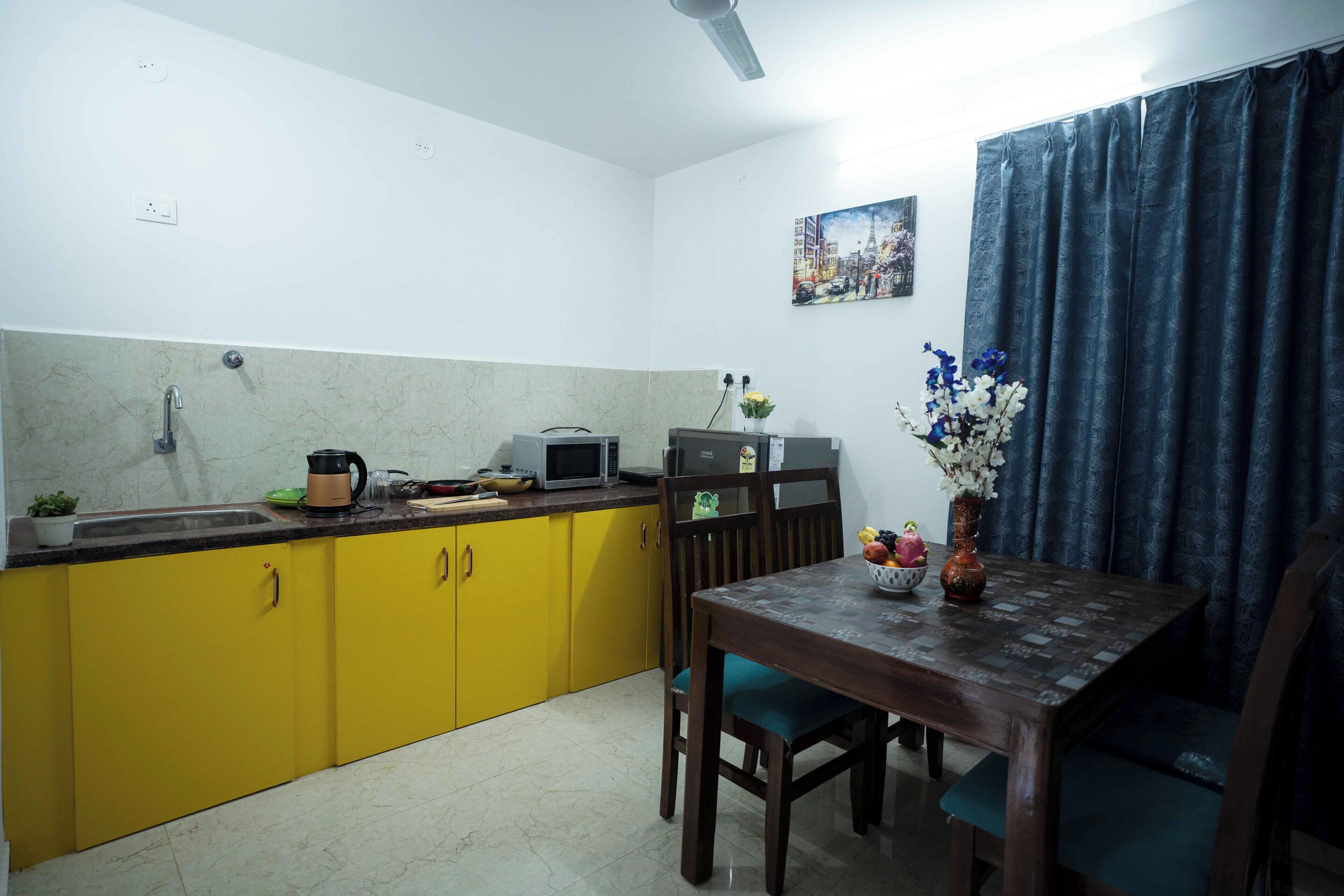 Une cuisine de taille réduite avec des meubles de couleur jaune, une table à manger et un rideau bleu.
