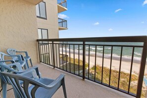 A balcony with a view of the beach and ocean, featuring plastic chairs and a railing.
