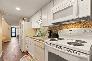 A kitchen with white appliances, a microwave, a stove, and a coffee maker. - Buena Vista #803 (North Myrtle Beach)