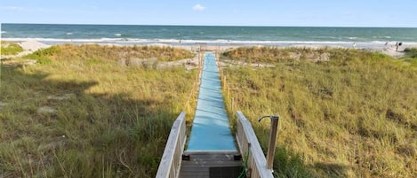A wooden boardwalk leading to a beach with a clear sky.