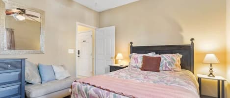 Un dormitorio con cama, tocador, espejo, puerta y mesita de noche con lámpara.