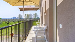 A balcony with a table and chairs, a yellow umbrella, and a view of a garden. - Regarda - Lagobaldo Studio with pool and garden (Lazise)