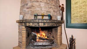 Una chimenea de ladrillo con fuego encendido, un estante con jarrones de vidrio de colores, y una escoba de madera apoyada contra la pared.