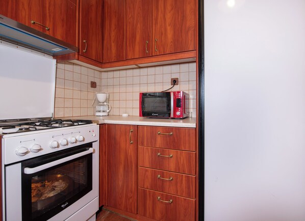 A kitchen with wooden cabinets, a gas stove, an oven, a microwave, and a coffee maker.