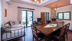 Un comedor espacioso con una mesa y sillas de madera, una chimenea y vistas al exterior a través de amplios ventanales.