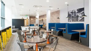 A modern restaurant with round tables and blue booths, featuring a brick wall and a cityscape mural. - Student Only Ablett House (Liverpool)