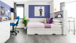 A modern bedroom with a bed, desk, chair, and a potted plant. - Student Only Ablett House (Liverpool)