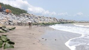 A sandy beach with large rocks and a person walking.