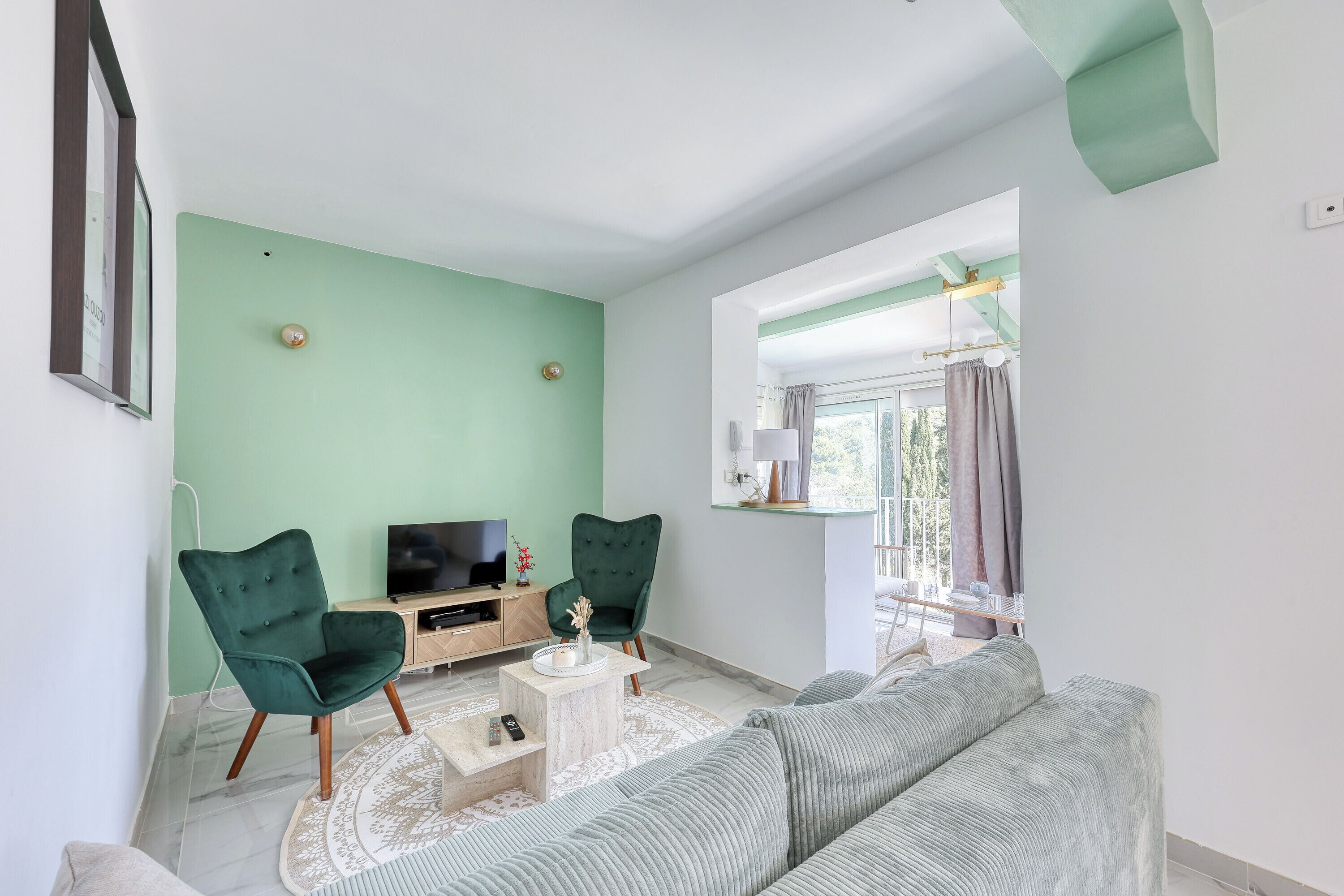A living room with a green wall, two green armchairs, a grey sofa, a TV on a wooden stand, and a small coffee table.