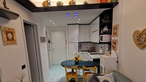 A compact living space with a dining area, kitchenette, and a sofa with decorative pillows. - Cozy Stay With Terrace and Shared Pool (San Michele al Tagliamento)
