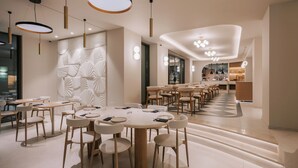 Un comedor moderno con mesas y sillas redondas, un muro decorativo y una escalera que conduce a otro nivel.