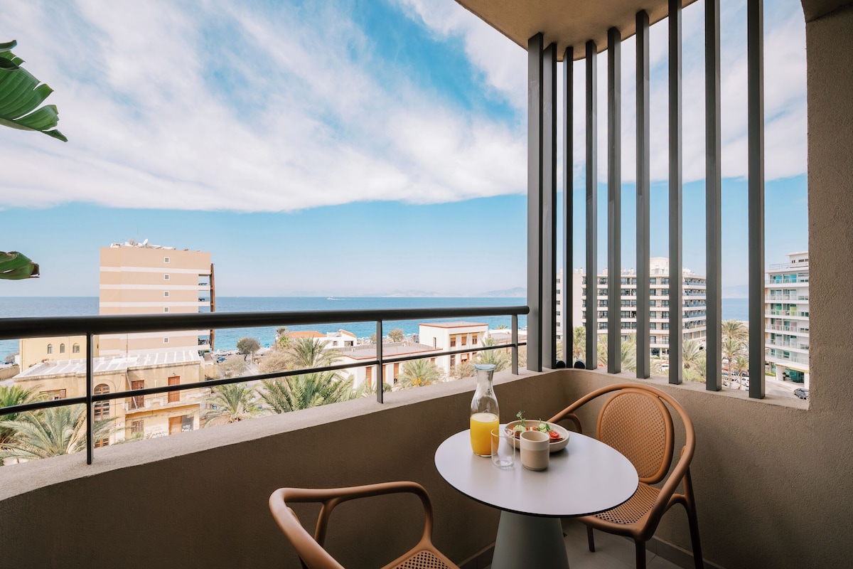 Un balcón con mesa y sillas, con vistas a un paisaje urbano costero.