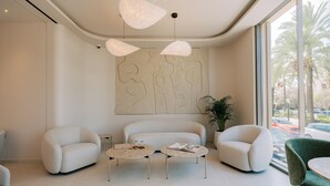 A modern lounge area with two round tables, three sofas, and a large abstract wall art piece. - Cento Palme (Rhodes)