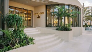 Una entrada de hotel moderna con fachada curva, un letrero que dice "CENTO PALME" y una escalera que conduce a la entrada.