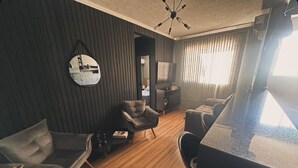 A modern living room with a dark wall, a round mirror, a sofa, a chair, a coffee table, and a television.